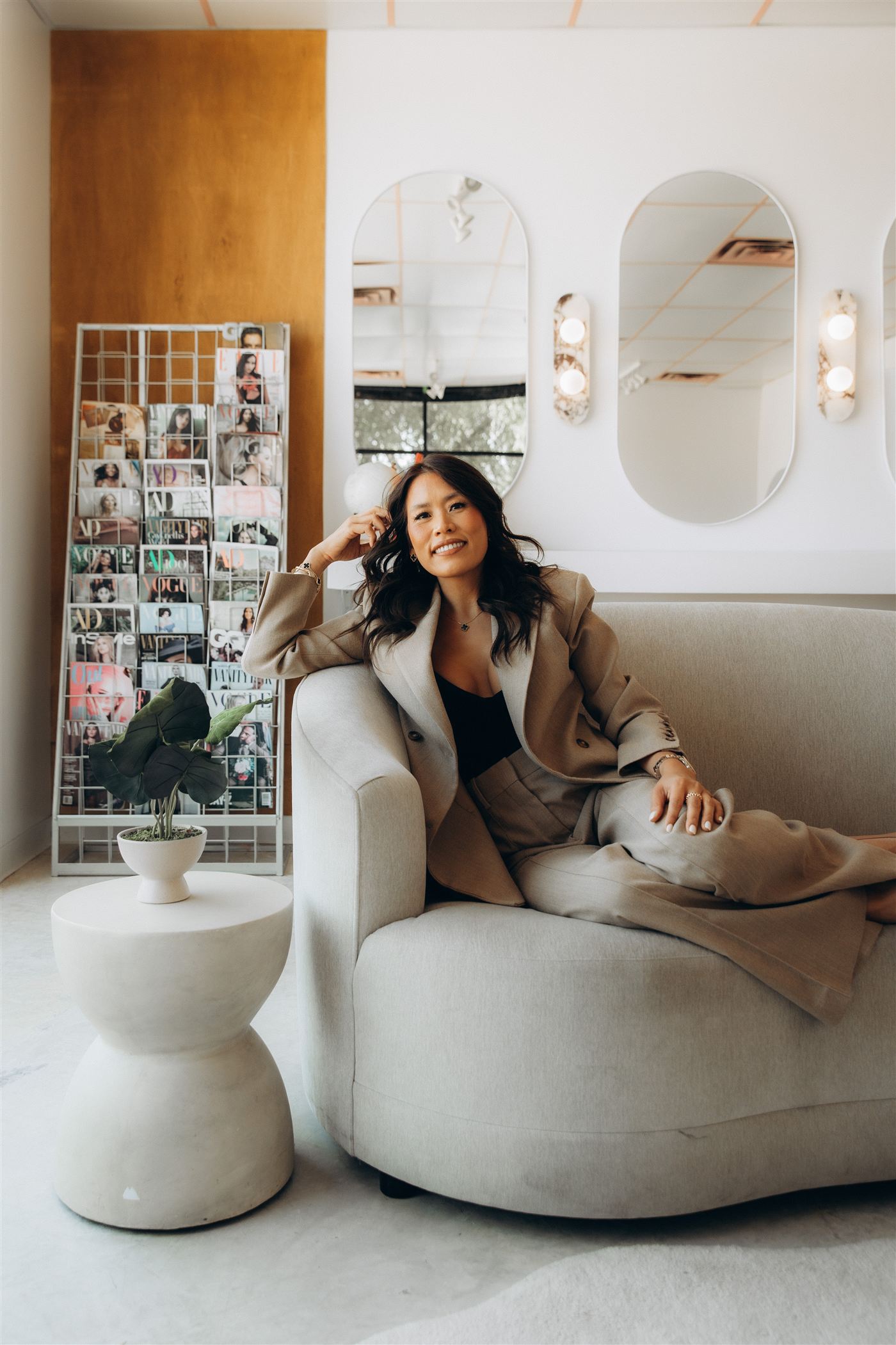 Anna Hong, smiling, seated on a sofa in a taupe suit