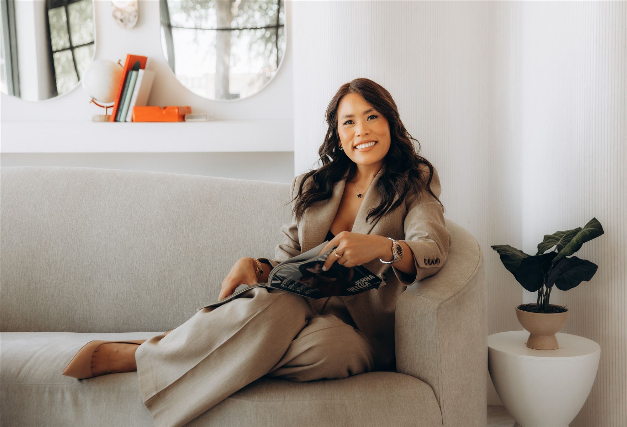 Anna Hong, smiling, seated on a sofa with a magazine