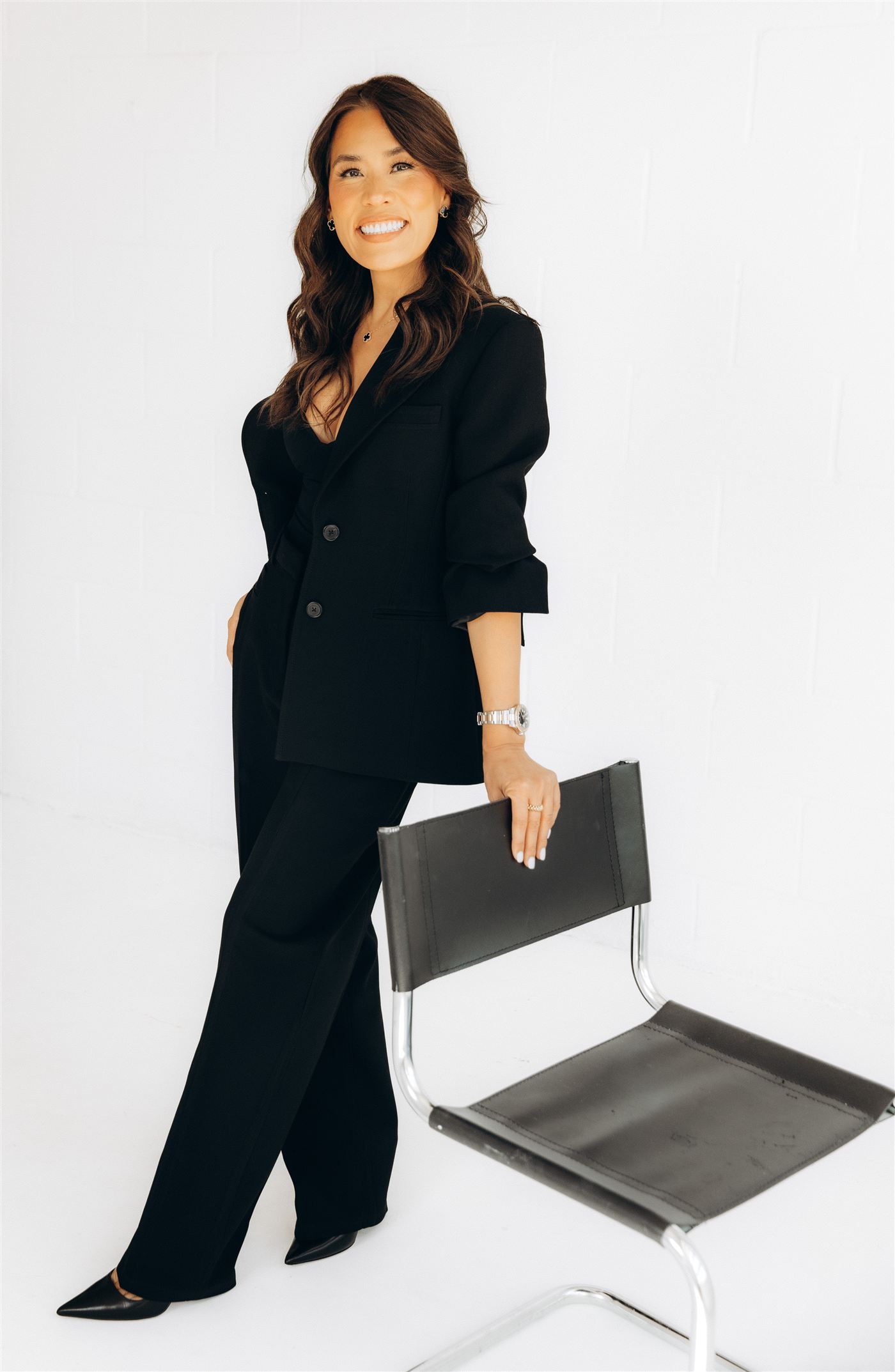 Anna Hong, smiling, standing in a black suit beside a chair